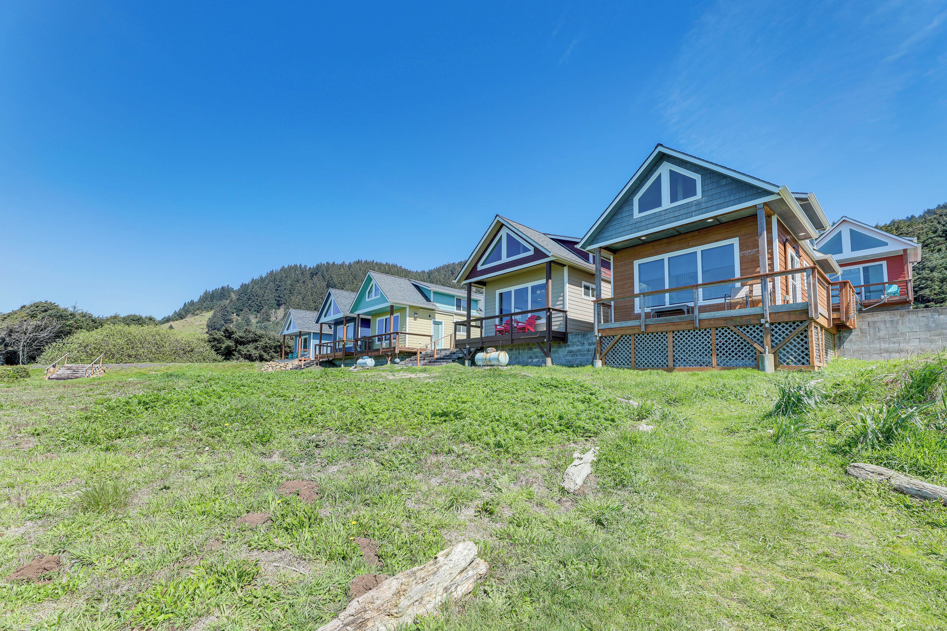 A row of modern cabins with large windows and a wooden exterior, set against a hillside backdrop.