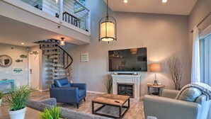 A modern living room with a staircase, a fireplace, a flat-screen TV, and a dining area. - Heated Pool, Steps to Beach: Indian Shores Condo! (Indian Shores)