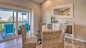 A dining area with wicker chairs, a glass table, and a white console table with a mirror and decorative items. - Heated Pool, Steps to Beach: Indian Shores Condo! (Indian Shores)