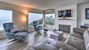 A modern living room with a large window, a gray sofa, a blue armchair, and a flat-screen TV mounted on the wall.