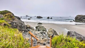 A coastal walkway leading to a beach with large rocks and grassy areas.