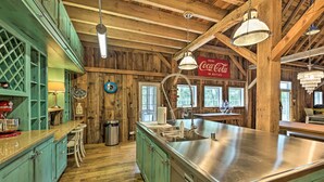 Una cocina rústica con vigas de madera, armarios verdes, una isla de acero inoxidable y un letrero de Coca-Cola.