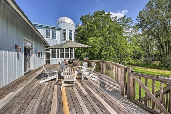 A wooden deck with Adirondack chairs and a table, a large blue building with a dome, and a wooden fence.