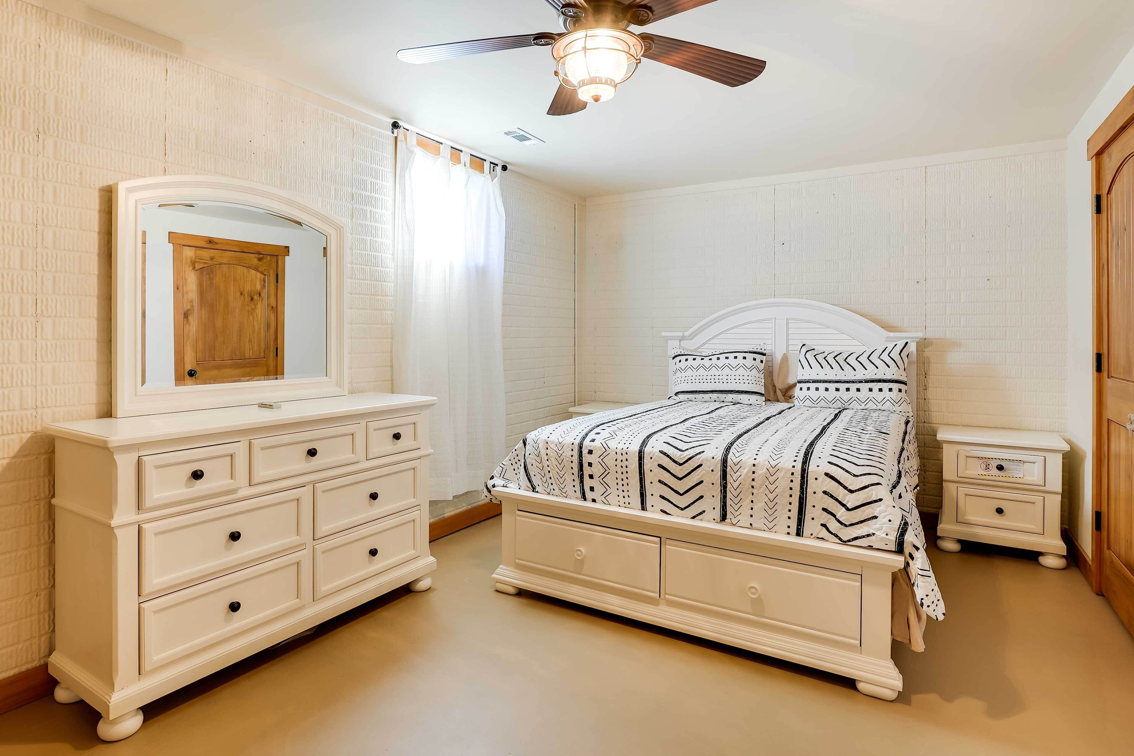 Un dormitorio con cama, cómoda, mesita de noche y ventilador de techo.