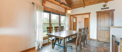 A dining area with a wooden table and chairs, a window with curtains, and a wooden ceiling.