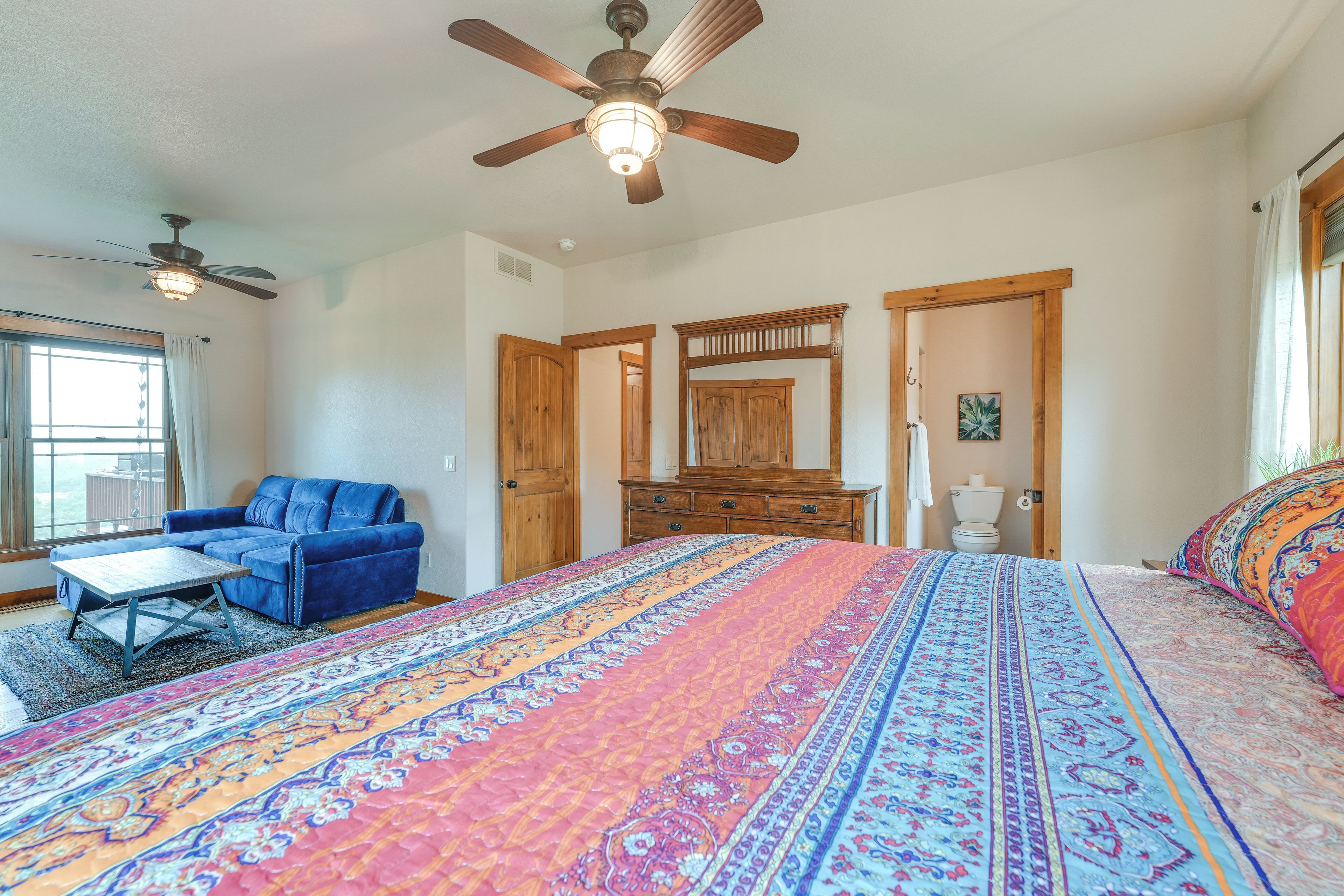 A bedroom with a large bed, a ceiling fan, a wooden dresser, and a blue sofa.