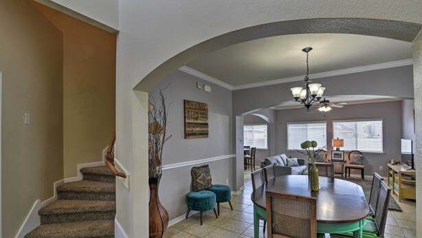 A spacious dining area with a large wooden table and chairs, a staircase with carpeted steps, and a chandelier.