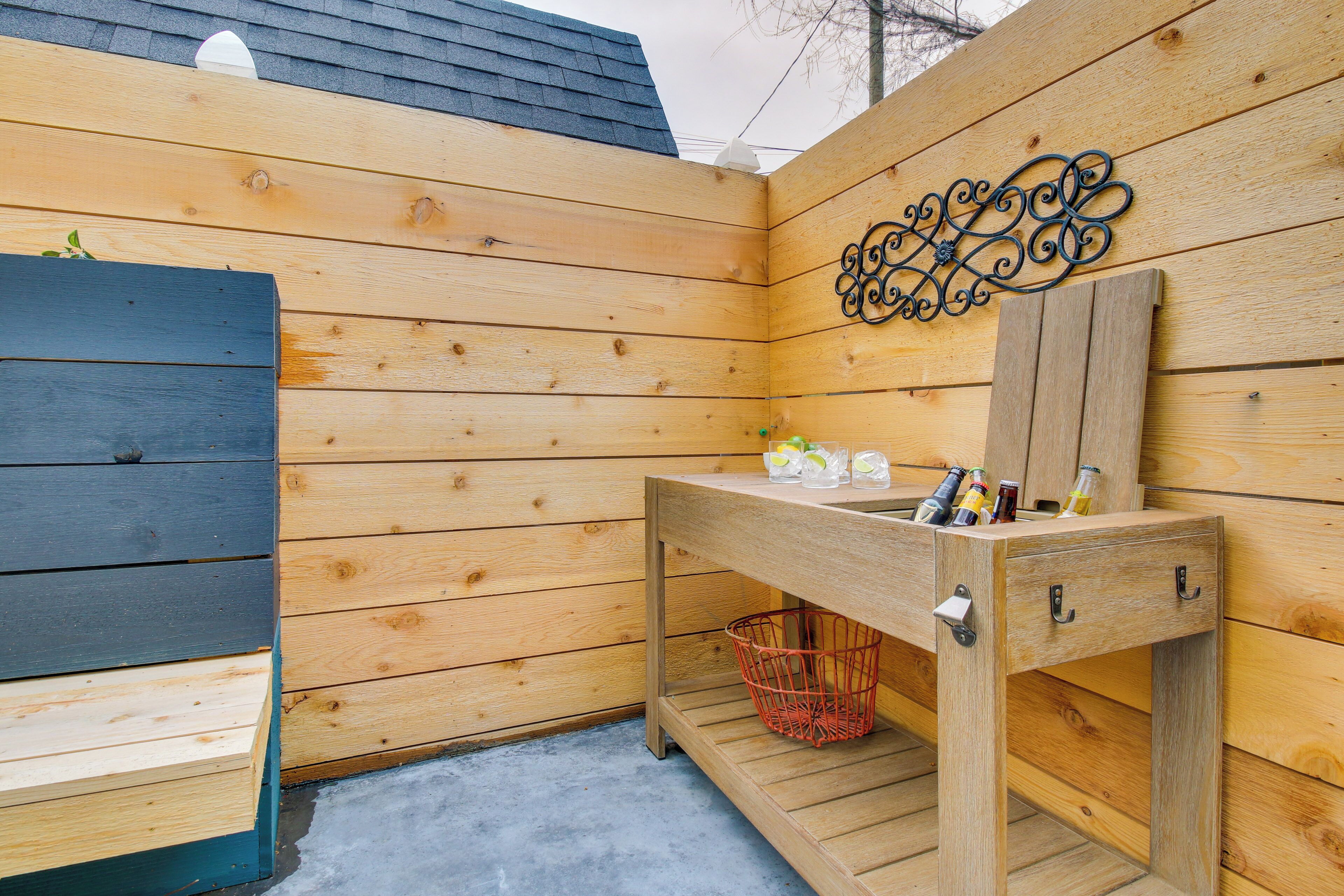 A wooden outdoor bathroom with a sink, storage drawers, and a decorative metal piece on the wall.