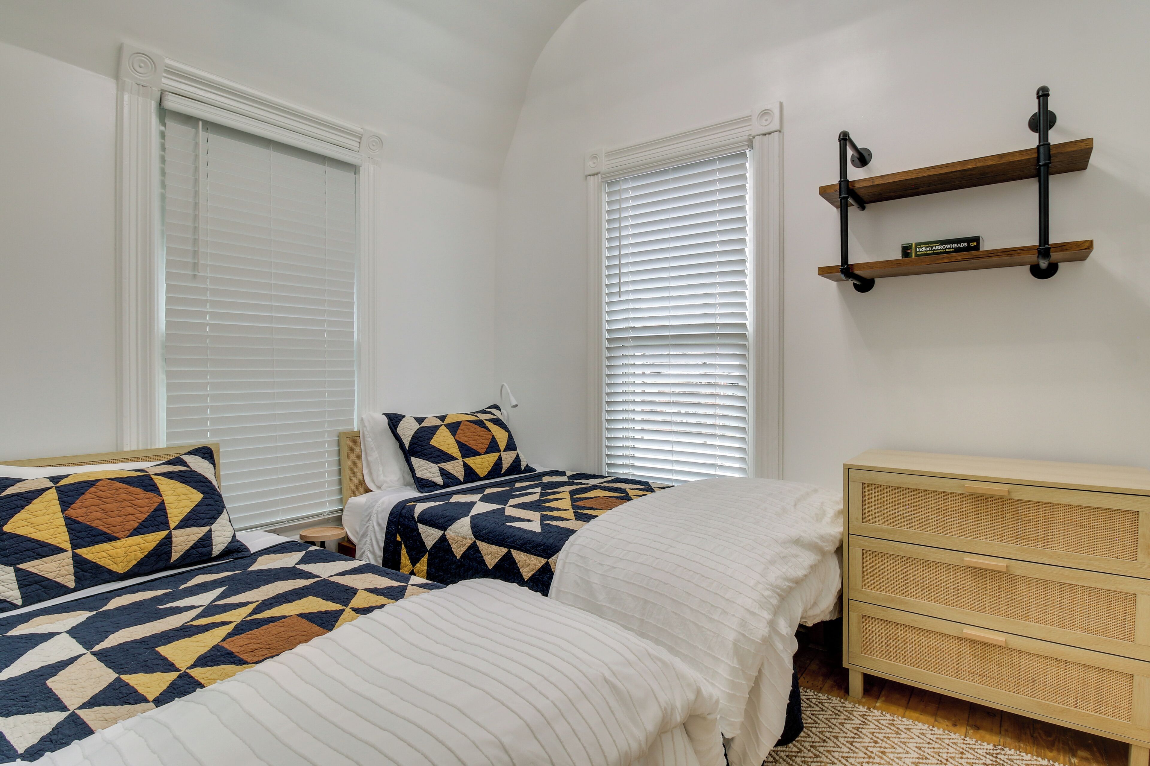 Un dormitorio con dos camas, ropa de cama blanca, un aparador de madera y un estante en la pared.