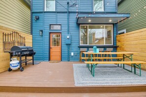 A blue house with a wooden deck, a barbecue grill, and a picnic table.