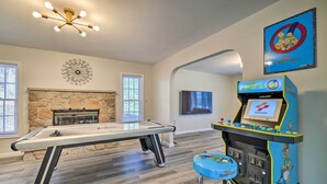 A pool table, a stone fireplace, and a The Simpsons arcade machine in a room with wooden flooring and white walls. - Movie Room, Hot Tub: Pocono Vacation Rental! (East Stroudsburg)
