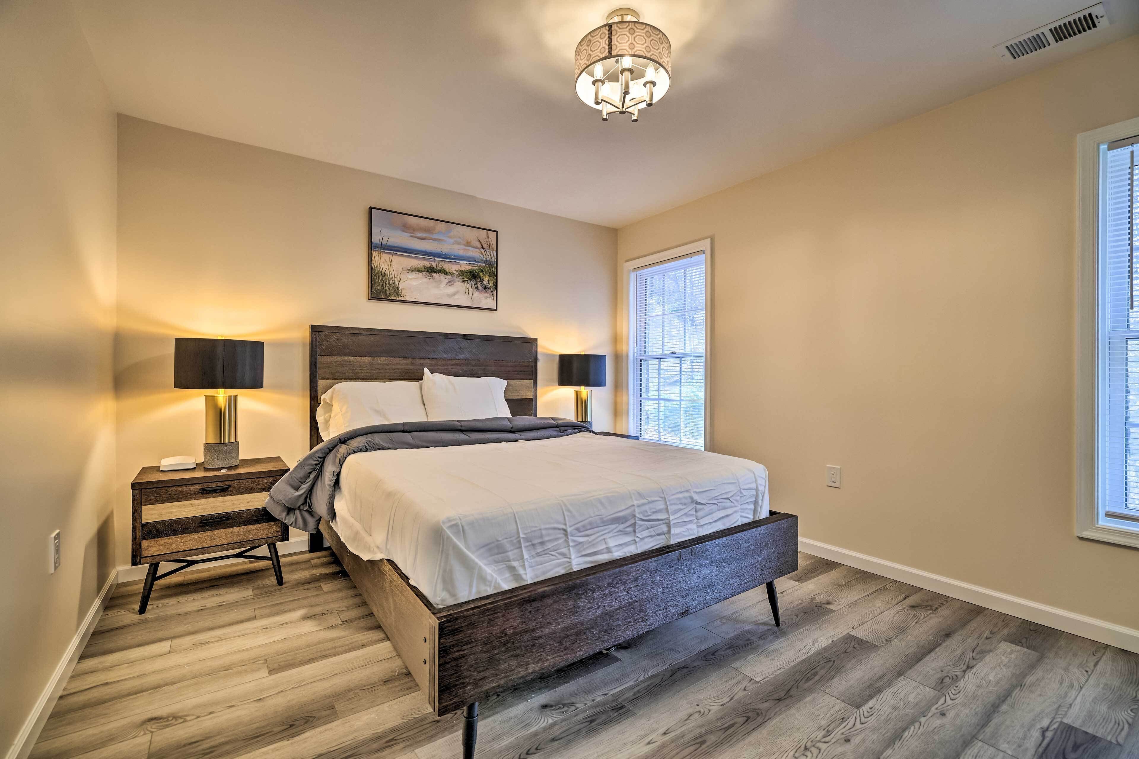 A bedroom with a large bed, two bedside tables with lamps, a ceiling light fixture, and a window with blinds.