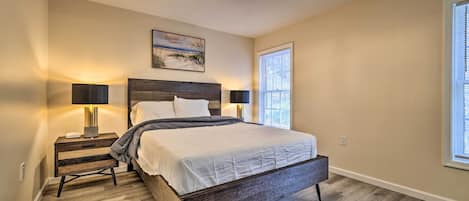 A bedroom with a large bed, two bedside tables with lamps, a ceiling light fixture, and a window with blinds.