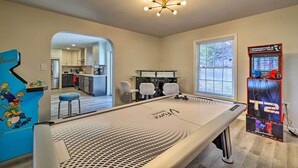 A modern kitchen with white cabinets, a stainless steel refrigerator, and a dining area with a long table and bar stools. - Movie Room, Hot Tub: Pocono Vacation Rental! (East Stroudsburg)
