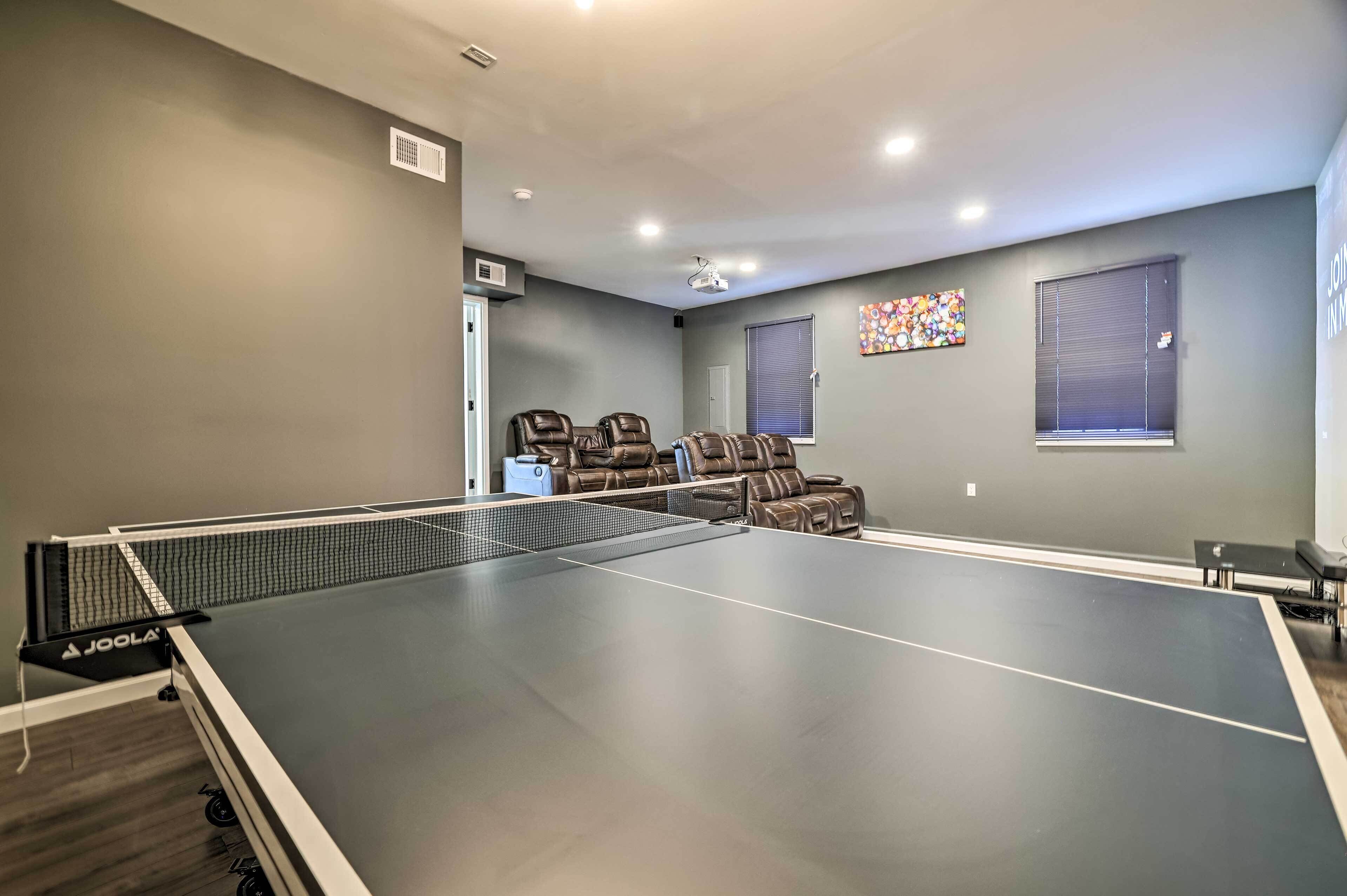 A room with a ping pong table, two leather recliners, a projector, and a window with blinds.