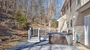 A patio with a hot tub, a wooden deck, and a house with a garage. - Movie Room, Hot Tub: Pocono Vacation Rental! (East Stroudsburg)