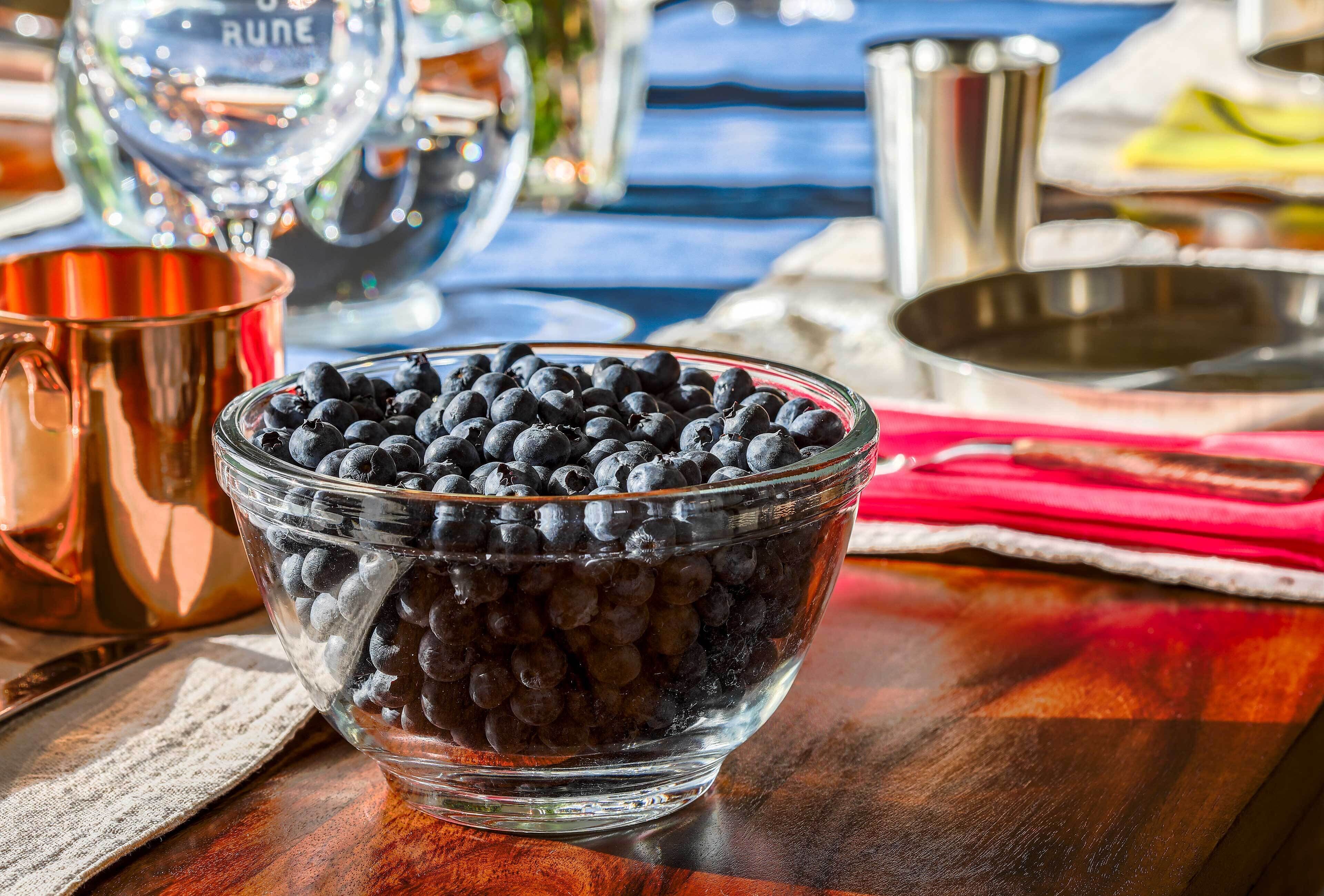 A glass bowl filled with blueberries on a wooden table.