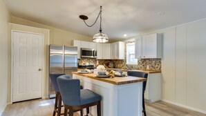 A modern kitchen with white cabinets, a stainless steel refrigerator, a microwave, and a wooden island with bar stools. - Walk to Lake! All-season Retreat in Poconos Mtns (Greentown)