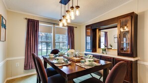 A dining room with a wooden table set for four, a large mirror above the table, and a view of the outdoors through the windows. - Walk to Lake! All-season Retreat in Poconos Mtns (Greentown)