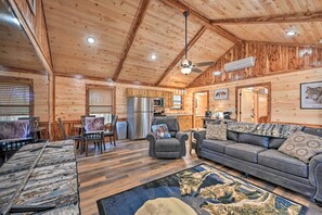 A log cabin interior with a dining area, kitchen, and seating with a fireplace.