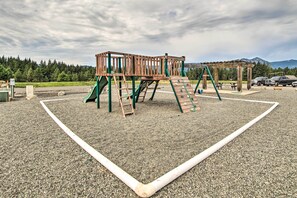 Une aire de jeux avec une structure d’escalade en bois, un toboggan et un espace pique-nique.