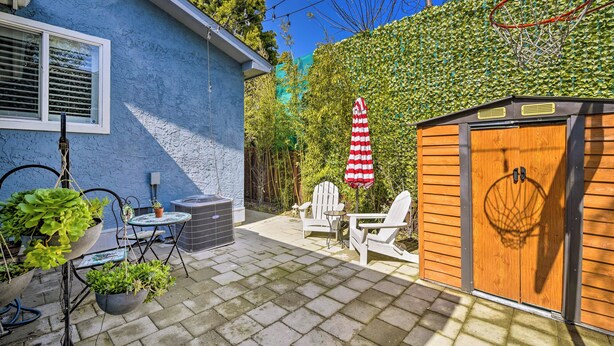 A backyard with a blue house, a wooden shed, a basketball hoop, outdoor furniture, and potted plants. - Bay Area Vacation Rental 4 Mi to Stanford! (Redwood City)