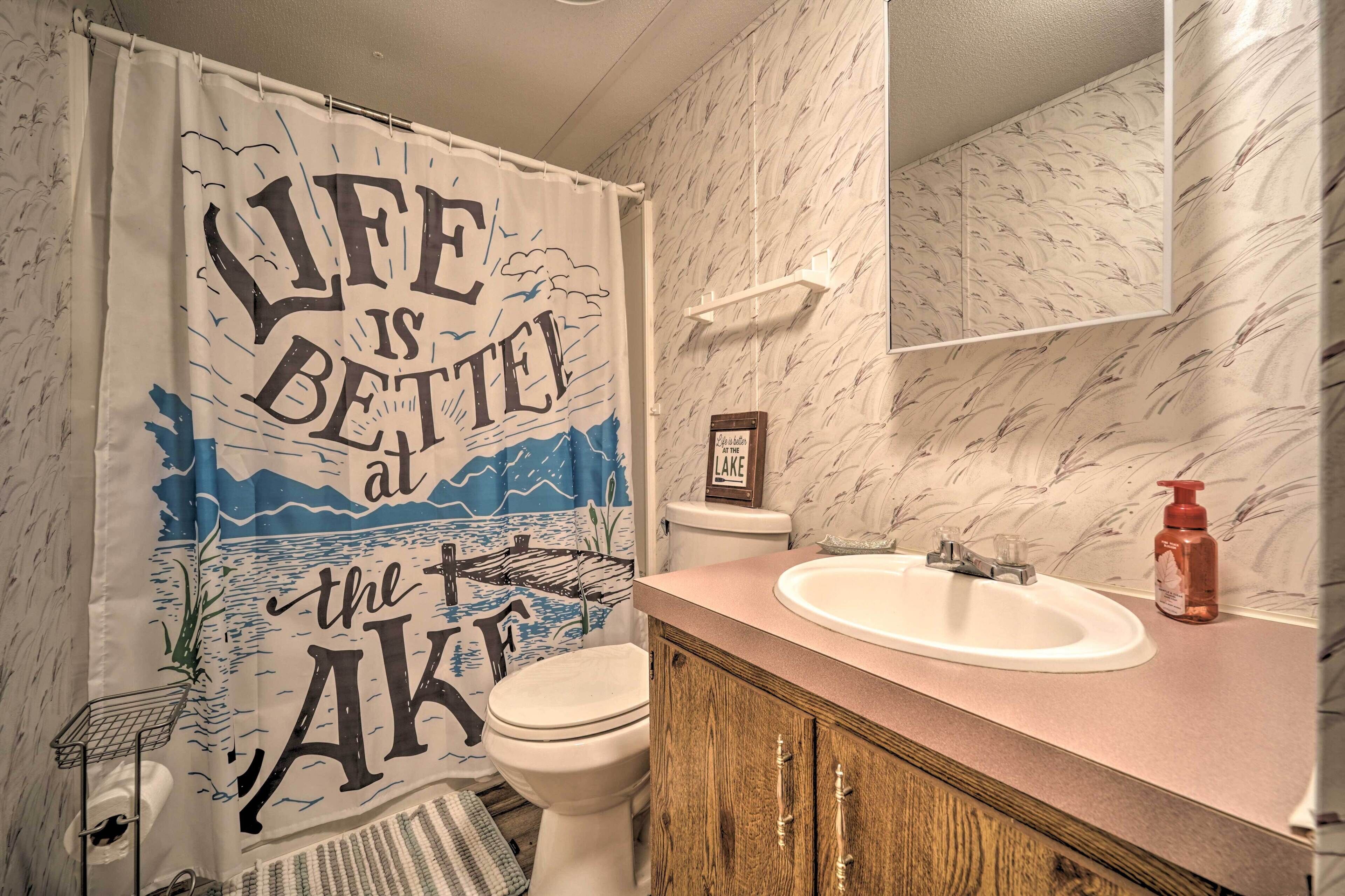 A bathroom with a toilet, sink, and shower curtain featuring a life is better at the AKI design.