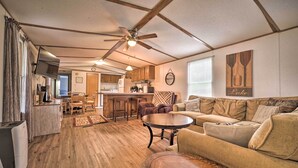 A spacious living area with a wooden floor, a sofa, a coffee table, and a kitchen in the background. - Quaint Cottage Overlooking Cherokee Reservoir (Bean Station)