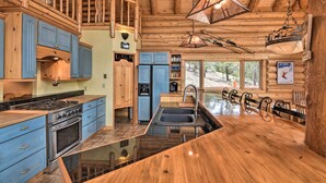 A spacious kitchen with wooden cabinets, a large island, and a view of the outdoors through large windows. - Spacious, Luxe Cabin w/ Mtn Views, Sauna & More! (Villa Grove)