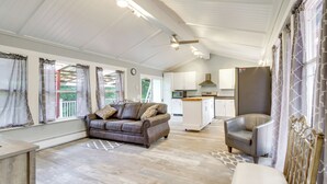 A spacious living area with a brown leather sofa, a white armchair, and a dining table. A kitchen with white cabinets and a refrigerator is visible in the background. - Cozy North Bend Getaway Near Dunes + Ocean! (North Bend)