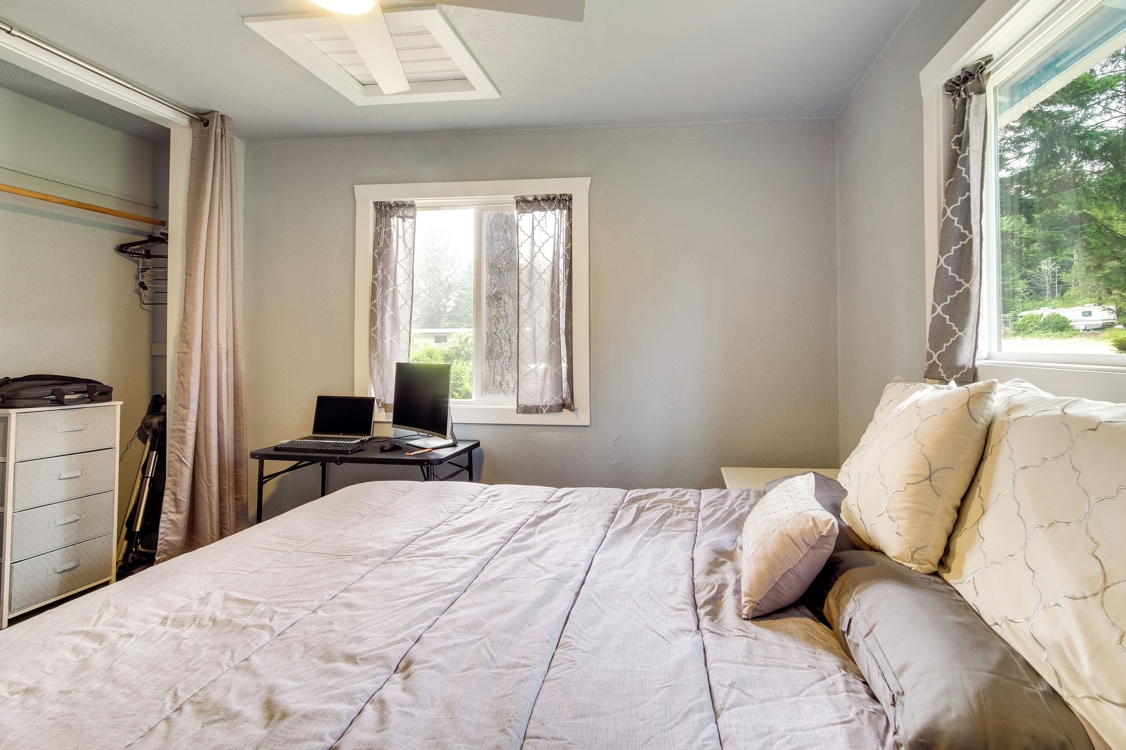 Un dormitorio con cama, escritorio, laptop, una silla y ventana con cortinas.