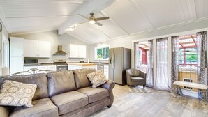 A spacious living area with a leather sofa, a bench, and a dining table. A kitchen with white cabinets and a refrigerator is visible in the background. - Cozy North Bend Getaway Near Dunes + Ocean! (North Bend)