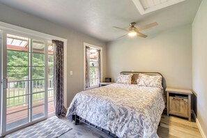 A bedroom with a large bed, a ceiling fan, and a sliding glass door leading to a deck.