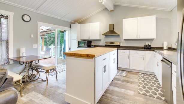 A modern kitchen with white cabinetry, a wooden island, and a dining area with a table and chairs. - Cozy North Bend Getaway Near Dunes + Ocean! (North Bend)