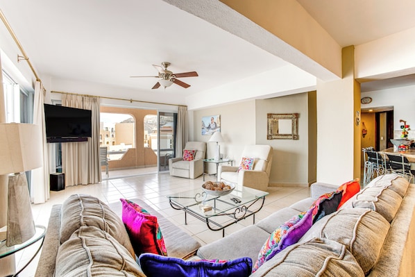 A living room with a sofa, coffee table, TV, and a ceiling fan. - Condo in Plaza Nautica < 1 Mile to The Arch! (Cabo San Lucas)