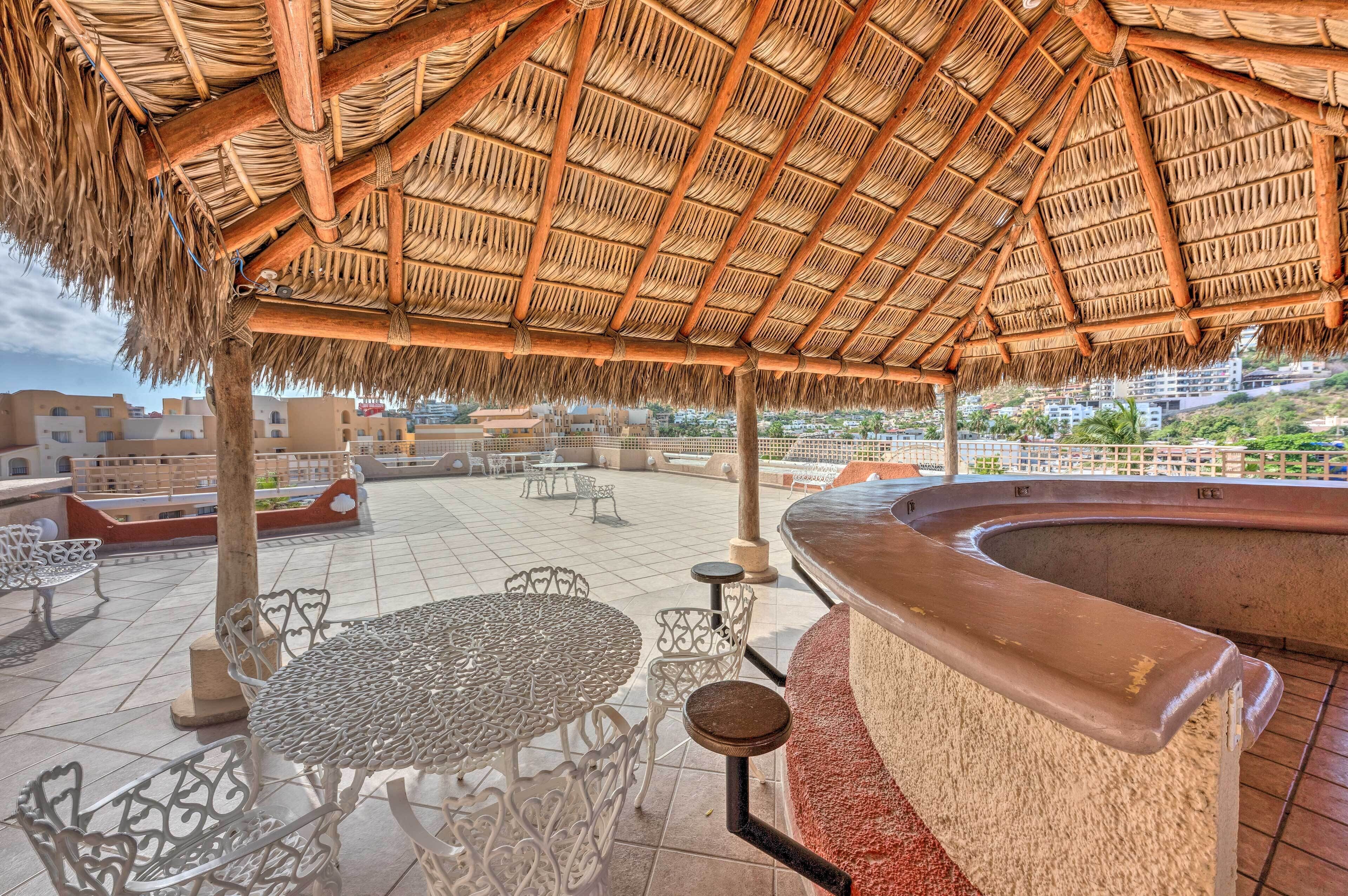 An outdoor patio with thatched roof, white metal tables and chairs, and a curved bar area.
