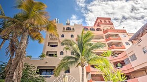 Un hotel de varios pisos con balcones, palmeras y un cielo azul despejado.