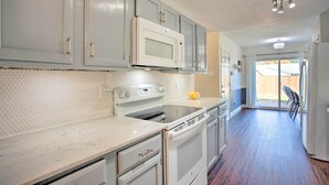 A kitchen with grey cabinets, a white microwave, a stove, and a sink.
