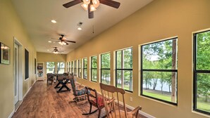 A long, open room with wooden flooring, multiple rocking chairs, and large windows offering views of a lake and trees. - Lakefront 'rest-ashored' Home w/ Private Dock! (Eddyville)