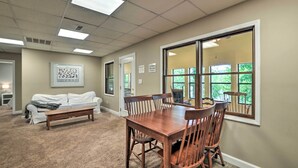 A spacious room with a large dining table and chairs, a white couch, and a bench. There is a large window with a view of greenery outside. - Lakefront 'rest-ashored' Home w/ Private Dock! (Eddyville)