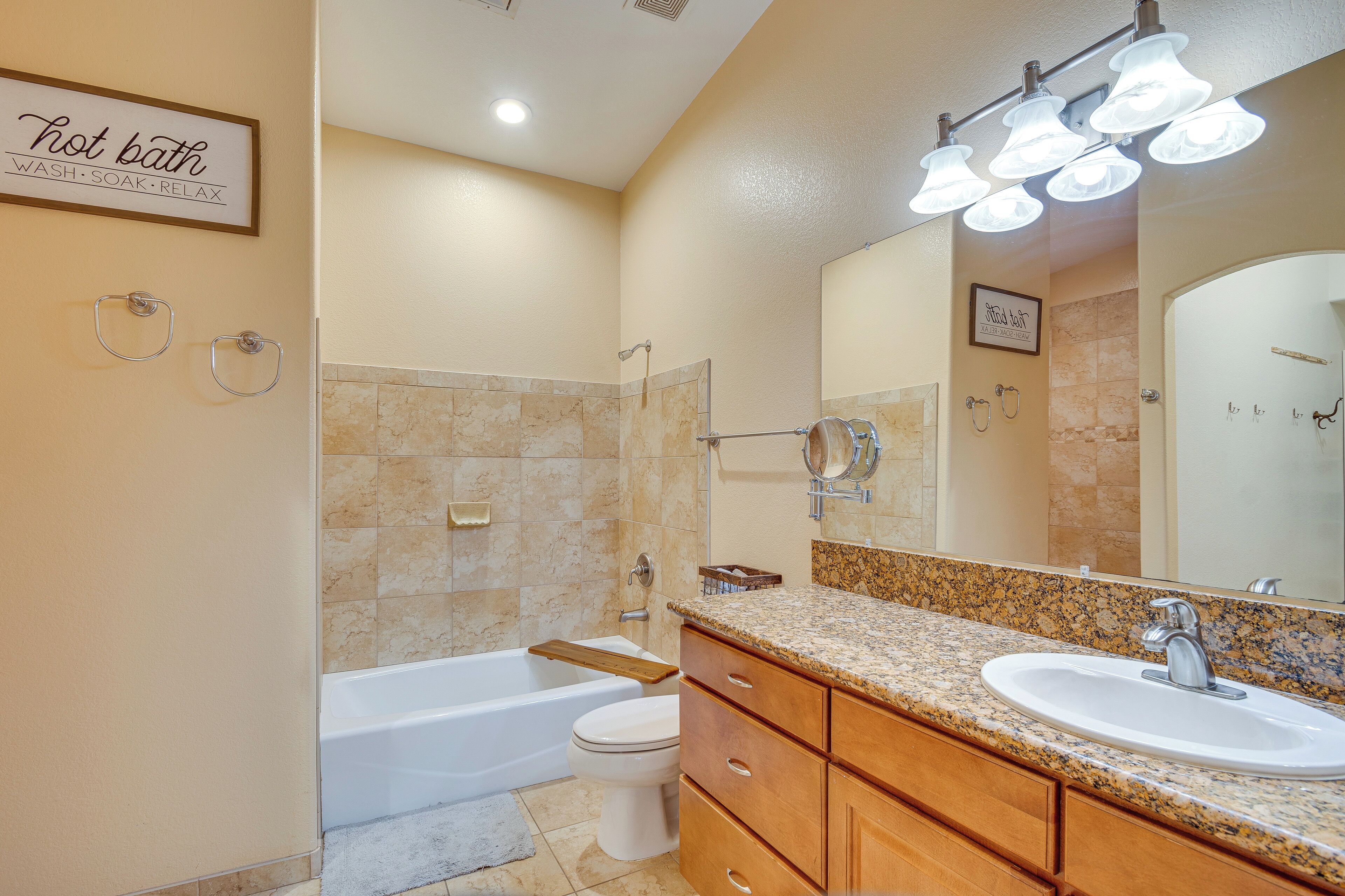 A bathroom with a bathtub, toilet, vanity with a sink, and a large mirror.