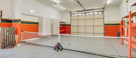 Pista de tenis con red, rodeada de paredes anaranjadas y color beige, y equipada con iluminación colgante.