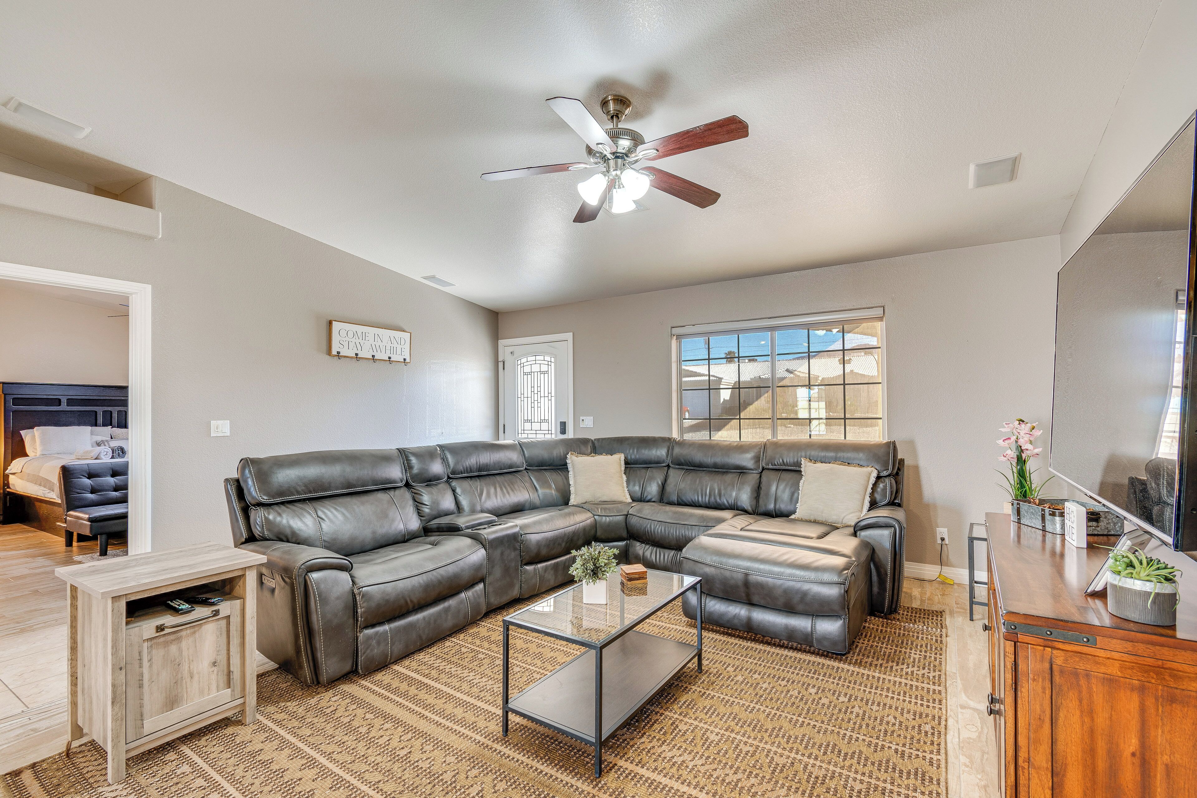 A living room with a sectional sofa, a glass coffee table, a ceiling fan, and a large window.