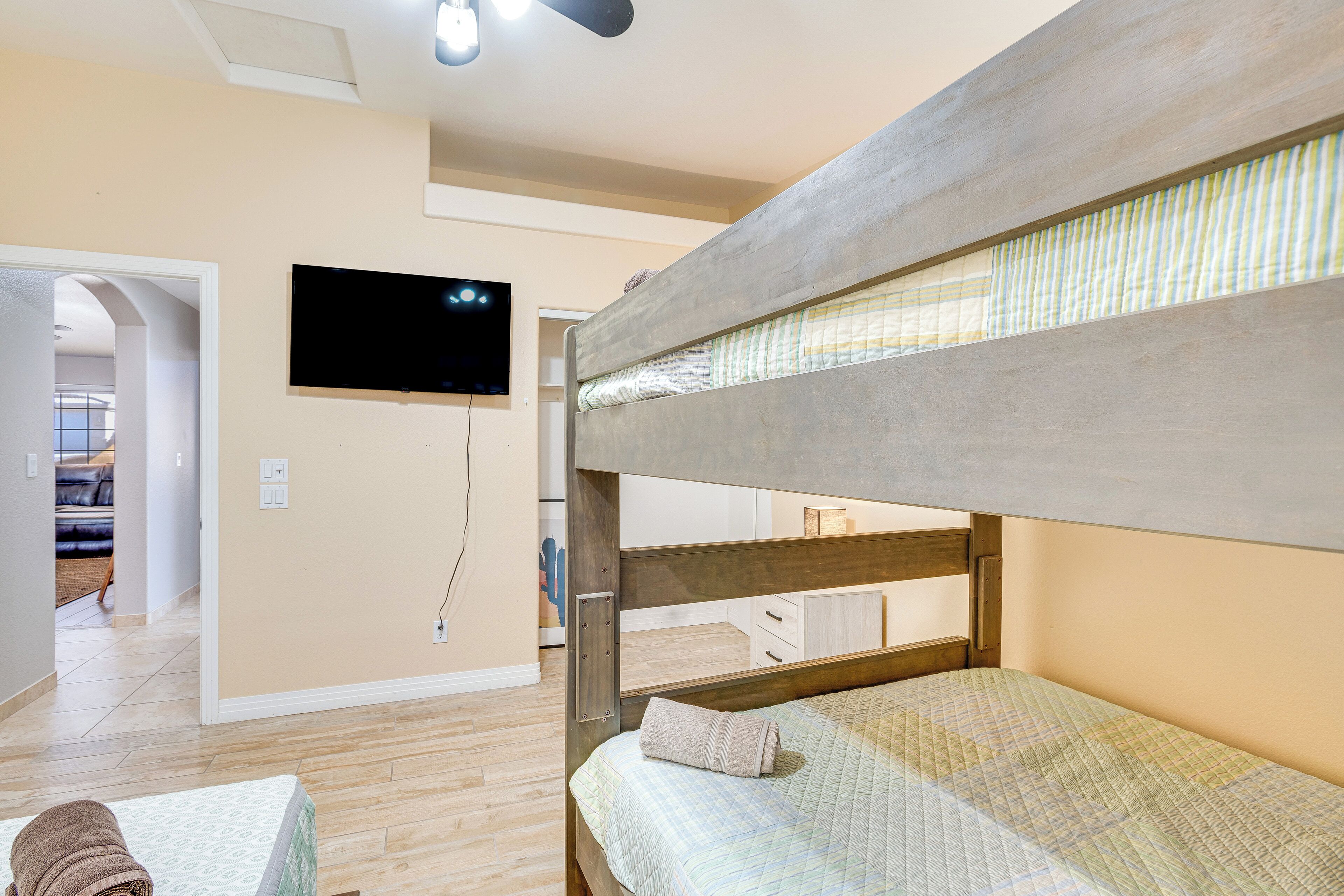 A bunk bed with a television mounted on the wall, a wooden floor, and a hallway leading to another room.