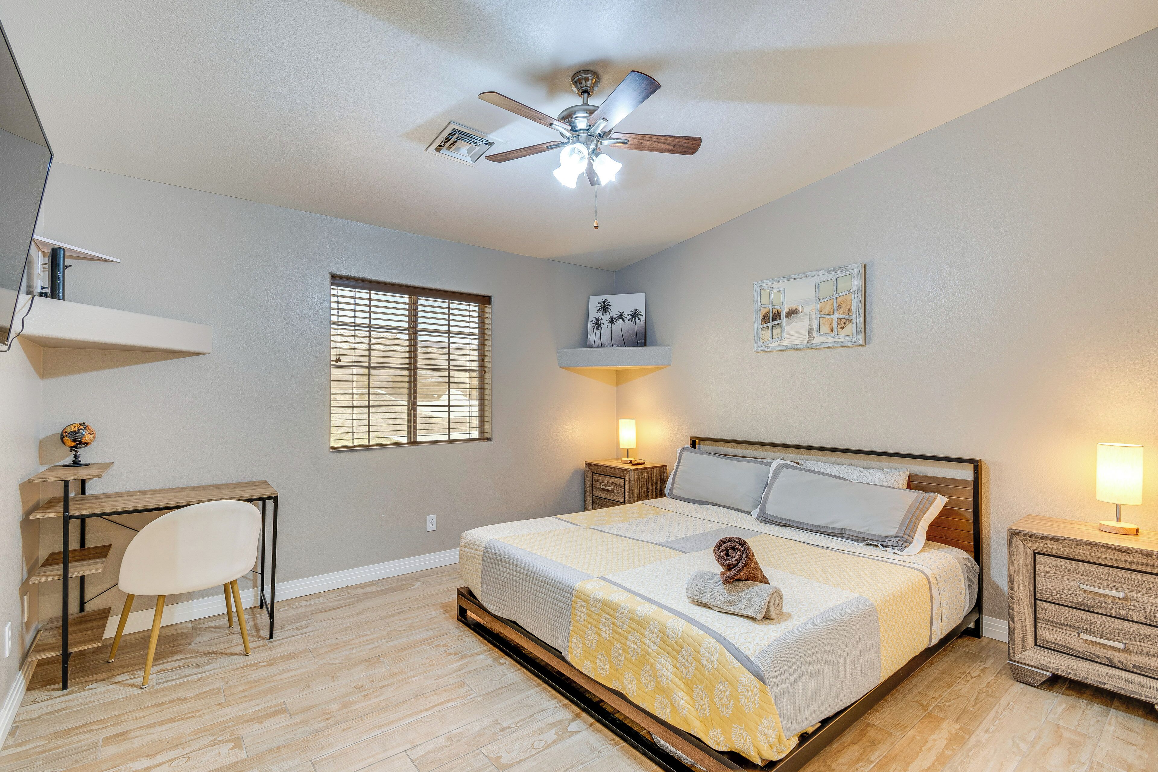 Une chambre à coucher comprenant un lit, un bureau, une chaise, un ventilateur de plafond et des œuvres d’art accrochées aux murs.