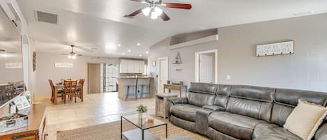 A spacious living room with a leather sofa, a dining area, and a kitchen in the background.