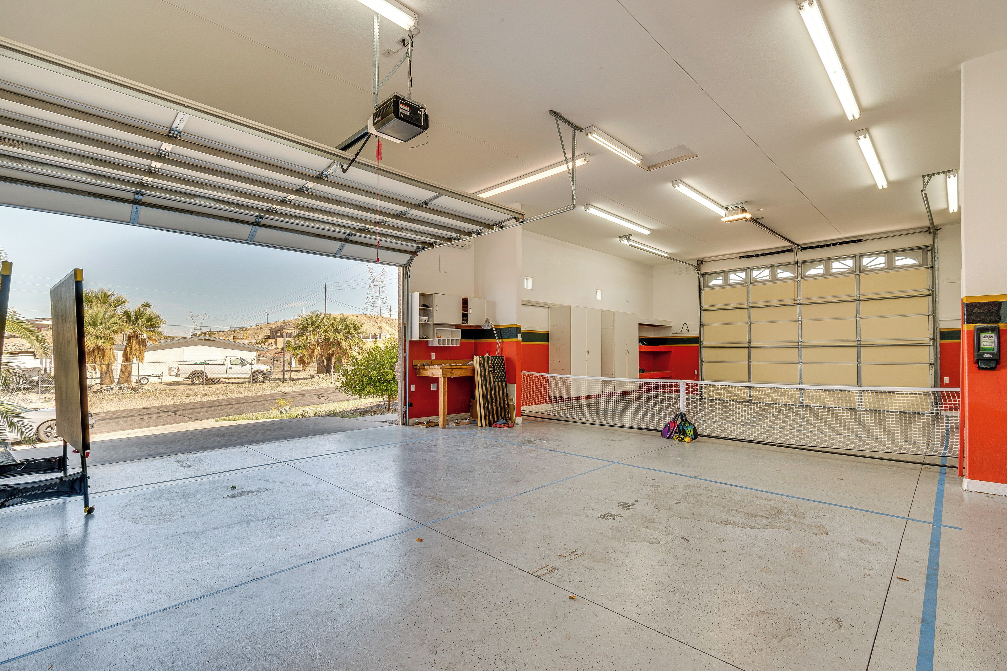 A covered tennis court with a net, a projector, and a garage door in the background.