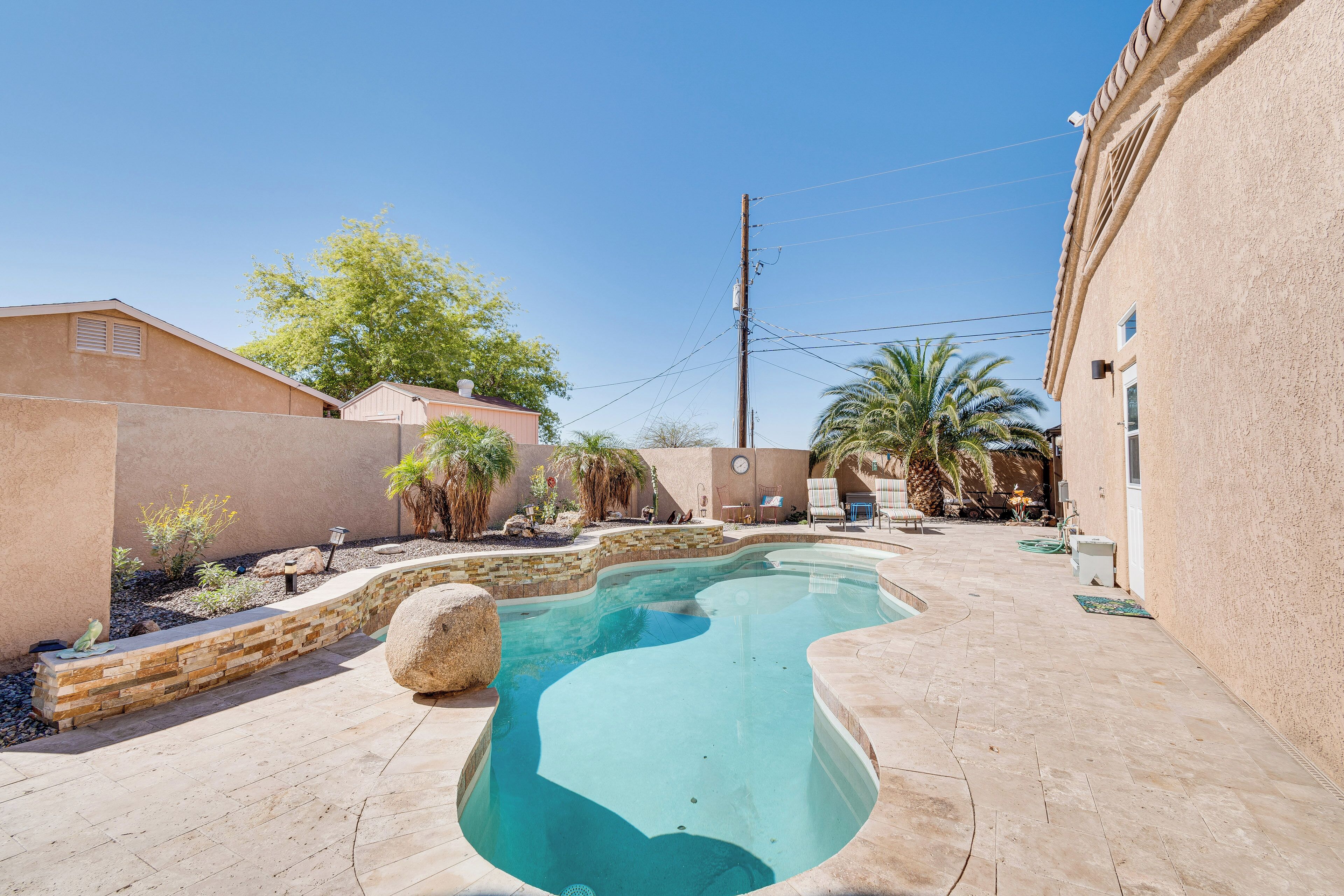 A swimming pool with a stone-lined edge, surrounded by a patio area with a stone floor and a few plants.