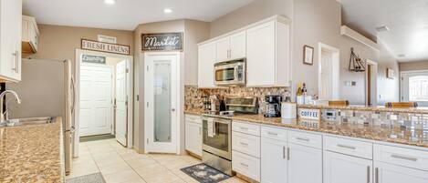 A kitchen with white cabinets, a granite countertop, stainless steel appliances, and a sign indicating a market and laundry area.
