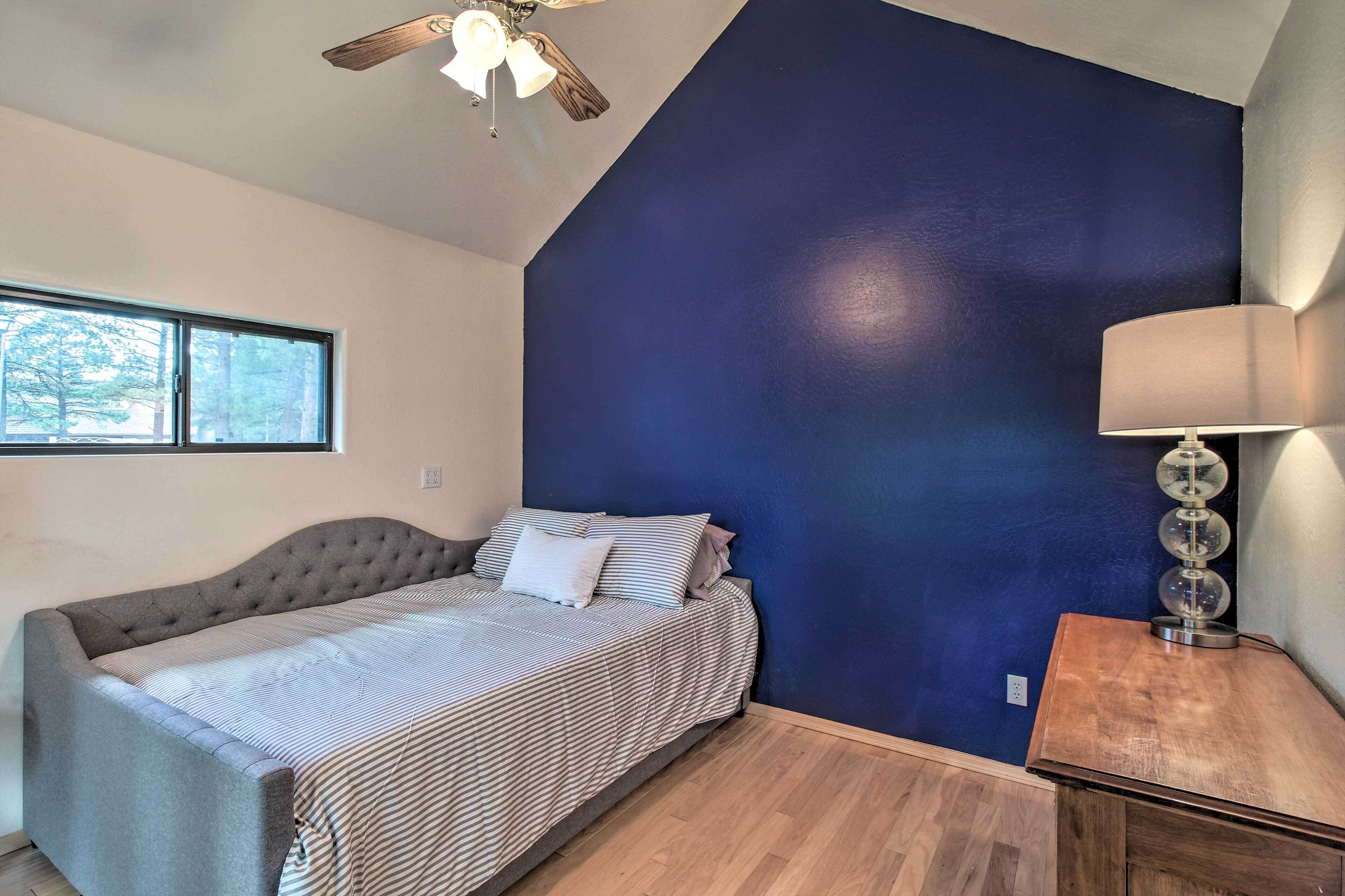 A bedroom with a bed, a ceiling fan, a window, and a nightstand with a lamp.